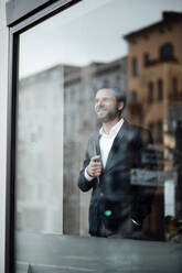 Businessman with hand pockets looking through window at office - GUSF06022