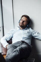 Businessman with headphones looking away while resting in office - GUSF06030