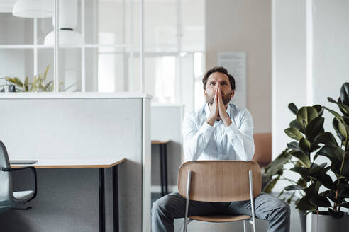 Businessman with hands clasped sitting on chair in office - GUSF06033