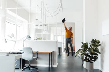 Businessman holding digital tablet while jumping in office - GUSF06043