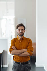 Smiling businessman with arms crossed standing in office - GUSF06044