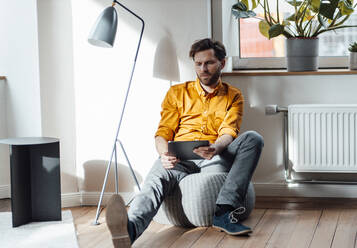 Businessman using digital tablet while sitting on hassock in office - GUSF06047