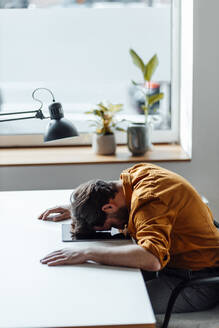 Businessman leaning on desk while sitting at office - GUSF06052