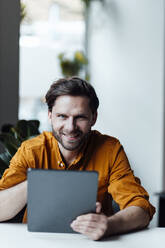Male entrepreneur with digital tablet smiling in office - GUSF06054