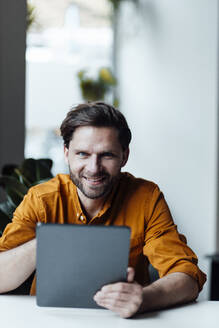 Männlicher Unternehmer mit digitalem Tablet lächelnd im Büro - GUSF06054