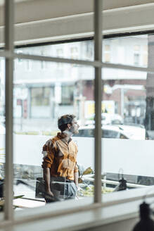Männlicher Unternehmer mit digitalem Tablet schaut durch ein Fenster im Büro - GUSF06057