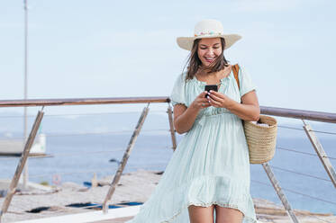 Lächelnde Frau, die am Geländer stehend eine Textnachricht über ihr Smartphone sendet - JCMF01982