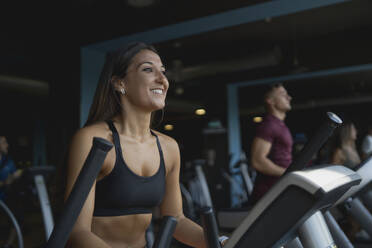 Lächelnde Sportlerin schaut weg, während sie auf dem Laufband im Fitnessstudio trainiert - MPPF01749