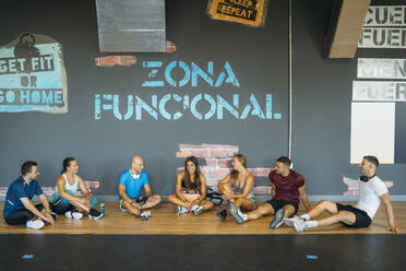 Lächelnde männliche und weibliche Freunde sitzen auf dem Boden im Fitnessstudio - MPPF01774