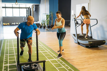 Frau überprüft die Zeit, während männliche und weibliche Sportler im Fitnessstudio trainieren - MPPF01778