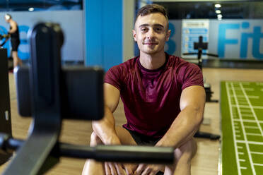 Handsome male athlete sitting on exercise equipment at gym - MPPF01782