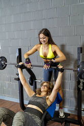 Lächelnde Sportlerin, die einem Freund beim Gewichtheben im Fitnessstudio hilft - MPPF01790