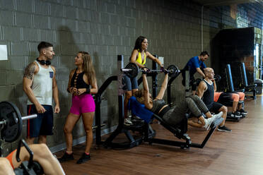 Woman talking with man while male and female friends exercising at gym - MPPF01792