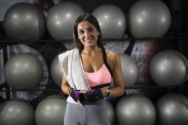 Lächelnde schöne Sportlerin mit Smartphone vor Fitnessbällen im Fitnessstudio stehend - MPPF01816