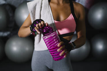 Sportlerin mit Wasserflasche vor Gymnastikbällen im Fitnessstudio stehend - MPPF01817