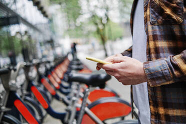 Junger Mann benutzt sein Smartphone an einer Fahrradparkstation - ASGF00424