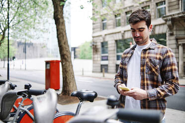 Young man using mobile phone at bicycle parking station - ASGF00426