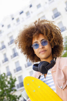 Junge Afroamerikanerin mit Kopfhörern und gelbem Skateboard - IFRF00747