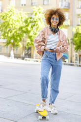 Smiling young woman with skateboard and mobile phone on footpath - IFRF00752