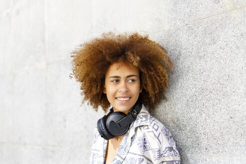 Junge Afro-Frau mit Kopfhörern vor einer Wand - IFRF00756