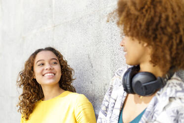 Smiling young woman looking at female friend in front of wall - IFRF00758