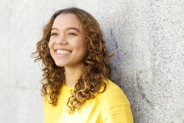 Smiling young woman day dreaming in front of wall - IFRF00763