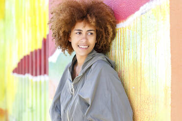 Lächelnde junge Frau, die wegschaut und sich an eine bunte Wand lehnt - IFRF00766