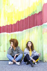 Junge Freundinnen schauen vor einer bunten Wand weg - IFRF00770