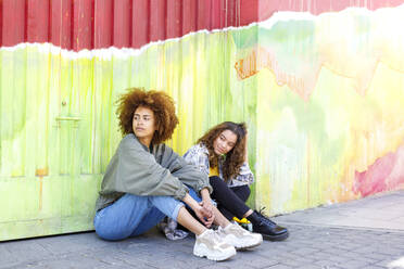 Zwei junge Freundinnen schauen weg, während sie auf dem Fußweg sitzen - IFRF00772