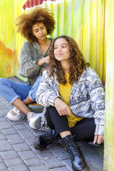 Afro woman adjusting female friends hair by multi colored wall - IFRF00777
