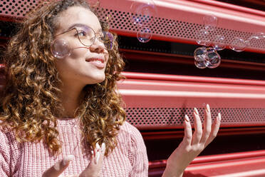 Lächelnde Frau spielt mit Seifenblasen an einem sonnigen Tag - IFRF00793