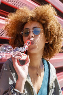 Afro young woman blowing bubbles on sunny day - IFRF00796