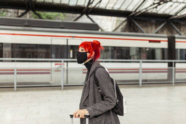Redheaded woman wearing protective face mask at railroad station - MRRF01224