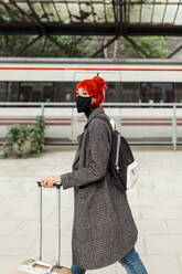 Redheaded woman wearing protective face mask walking at railroad station - MRRF01225