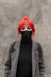 Redheaded woman wearing protective face mask standing in front of wall during COVID-19 - MRRF01237