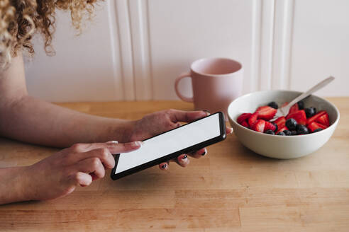 Frau benutzt Smartphone neben Obstschale in Küche zu Hause - EBBF03828