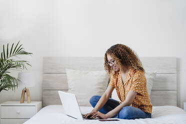 Smiling young woman using laptop on bed at home - EBBF03831