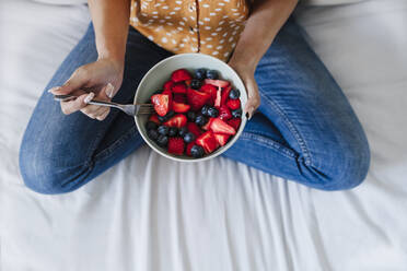 Woman having fresh berries on bed at home - EBBF03841