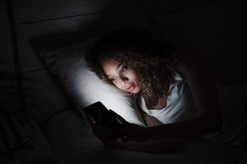 Frau benutzt Smartphone, während sie nachts im Bett liegt - EBBF03849