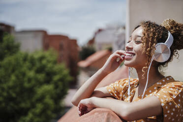 Happy woman with eyes closed listening music in balcony - EBBF03876