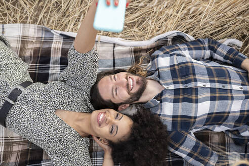 Lächelnde Frau nimmt Selfie durch Smartphone mit Mann, während auf der Decke liegend - JCCMF02786