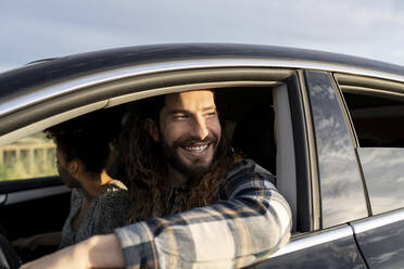 Mid adult man smiling while looking way in car - JCCMF02800