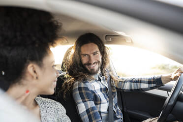 Smiling boyfriend looking at girlfriend while driving car - JCCMF02805