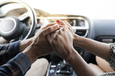 Mid adult couple holding hands while sitting in car - JCCMF02808