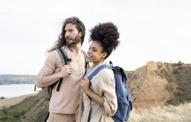 Couple with backpack smiling while looking away - JCCMF02811