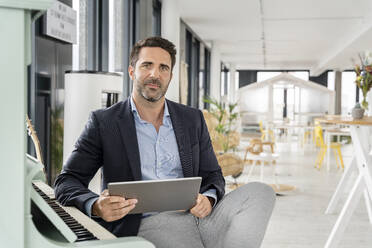 Geschäftsmann mit digitalem Tablet sitzt am Klavier in der Cafeteria im Büro - PESF02833