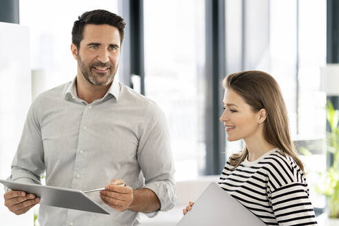 Lächelnder männlicher Fachmann, der wegschaut, während er mit einer Kollegin im Büro über ein digitales Tablet diskutiert - PESF02861
