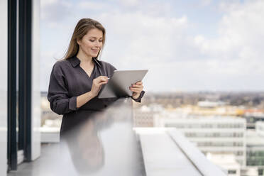 Smiling businesswoman using graphics tablet in balcony at office - PESF02876