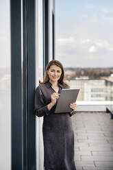 Smiling businesswoman with graphics tablet standing at balcony - PESF02878