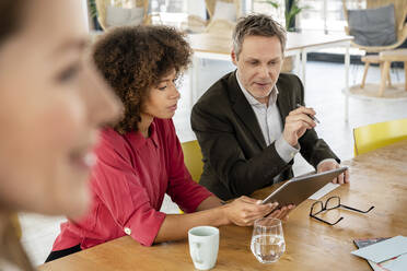 Male and female professionals discussing over graphics tablet at office - PESF02889